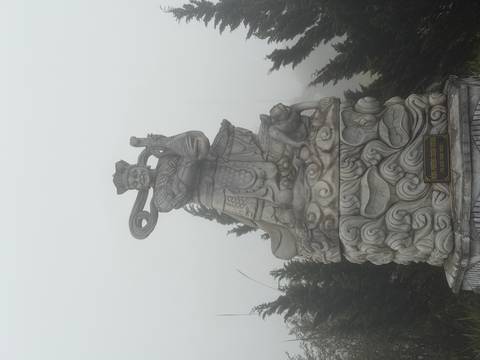       Stone warrior statue stands amid dense fog in a mountain setting.
  