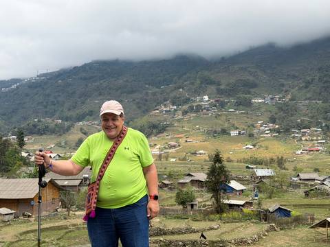       Traveller smiles on a hill overlooking scattered mountain villages beneath low clouds.
  