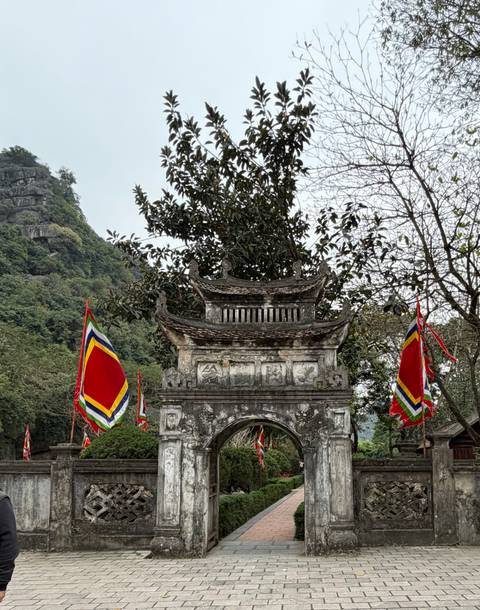       Ancient stone gate adorned with colorful flags set against lush cliffs.
  