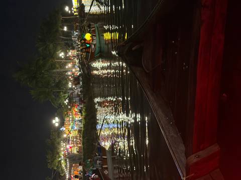      Nighttime view from a wooden boat on a lantern-lit river with reflections of colorful lights and busy riverbanks in Hoi An.
  