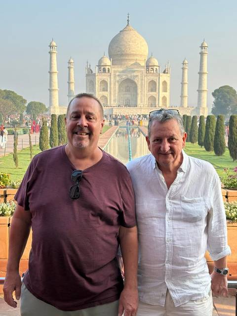       Two male tourists posing for a photo with the Taj Mahal and its reflecting pool in the background.
  