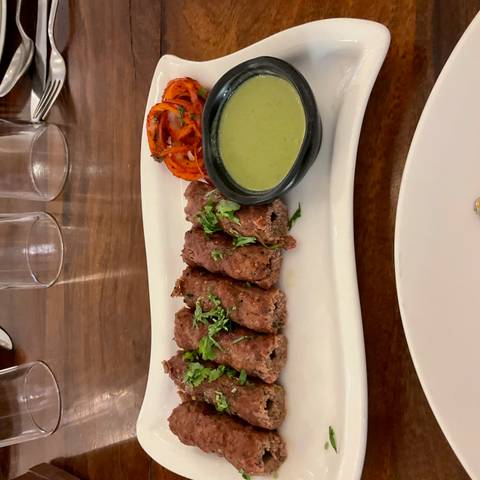       Platter of grilled minced-meat kebabs garnished with fresh herbs, served with green chutney and pickled onions.
  