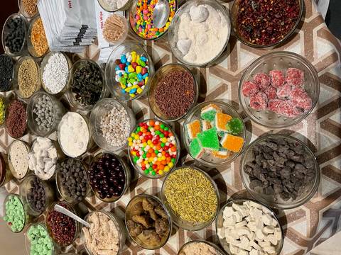       Assortment of colorful spices, sweets and dried goods displayed in glass bowls on a patterned table.
  