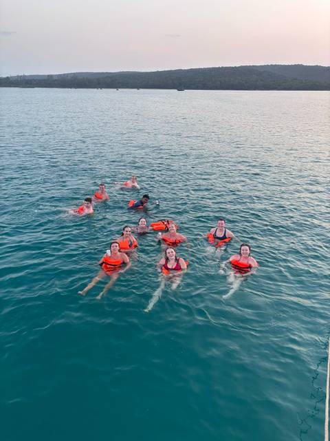       Smiling travellers wearing life jackets float together in clear blue sea water.
  