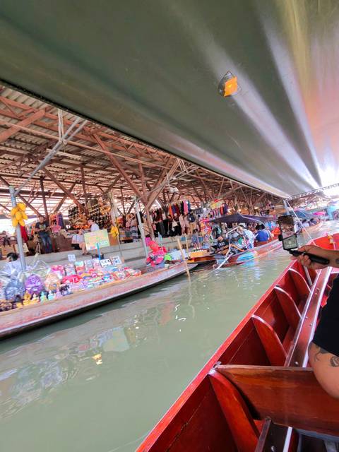      Bustling floating market scene viewed from a long-tail boat with stalls, souvenirs and paddling vendors.
  