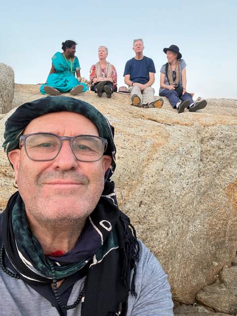       Close-up selfie of traveller wearing glasses and headscarf sitting on a granite boulder.
  