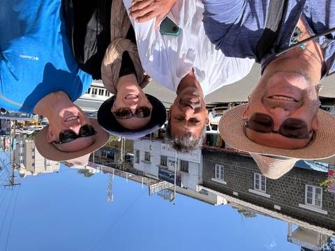       Travellers pose with their driver on a sunny street in a hill town shopping area.
  