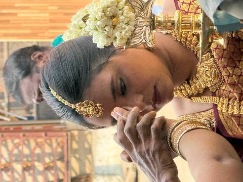       Close-up of bride having ritual mark placed on her forehead, adorned with ornate gold jewellery.
  