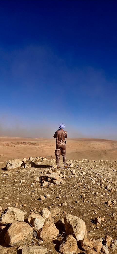       Traveller dressed in traditional robe gazing over vast desert panorama beneath clear blue sky
  