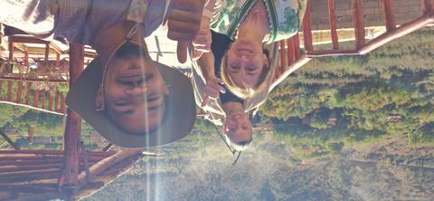       Three happy travellers giving thumbs up on a sunny terrace with valley backdrop and lens flare
  