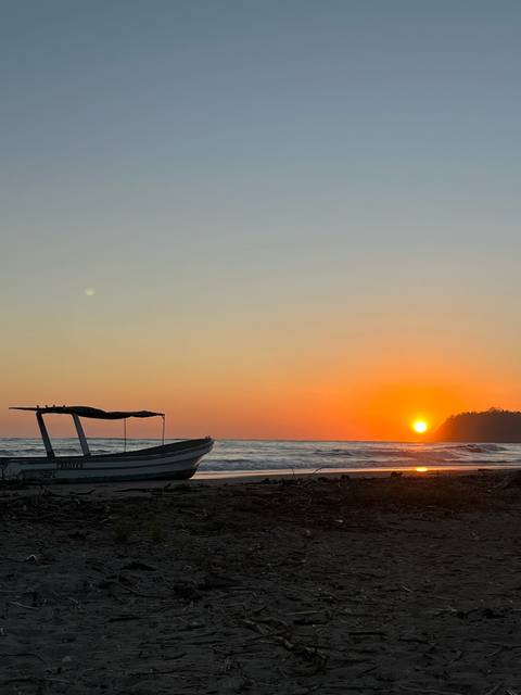       Silhouette of a small fishing boat on a quiet tropical beach at vivid orange sunset
  