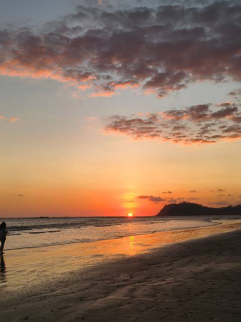       Brilliant orange sunset over the Pacific with the sun dipping below the horizon near a jungle-covered headland
  