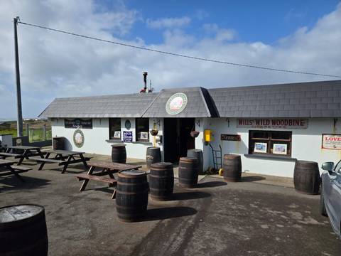       Small rural Irish pub with outdoor benches and wooden barrels under a partly cloudy sky
  