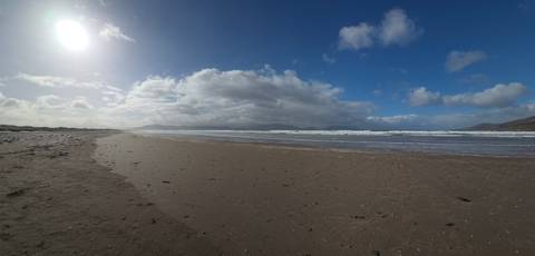       Wide sandy beach in Ireland with dramatic clouds, distant mountains and bright low sun
  