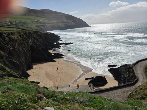       Rugged Irish coastline with sandy cove, cliffs and a winding path with a few visitors on the beach
  