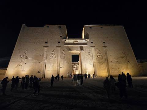       Night-time illumination of the Temple of Horus at Edfu with visitors silhouetted in front of the monumental façade
  