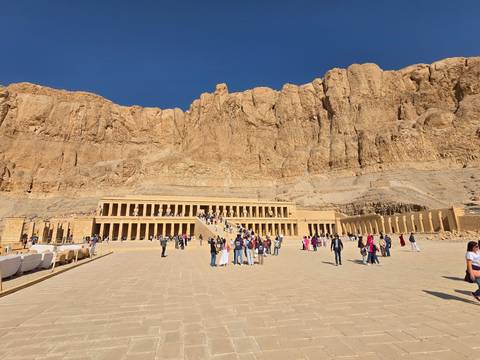       Terraced Temple of Hatshepsut set against towering sandstone cliffs with tourists walking on the plaza
  