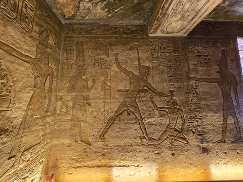       Detailed stone relief of a pharaoh striking a captive surrounded by hieroglyphs inside an ancient temple
  