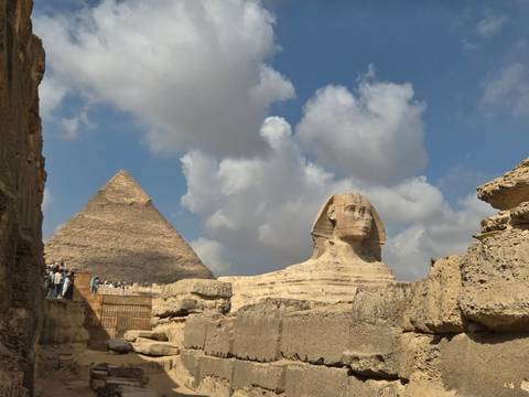       Front angle of the Sphinx with a pyramid backdrop and dramatic clouds in the sky
  