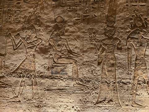       Close-up of sandstone wall carving of seated and standing Egyptian figures in warm light
  