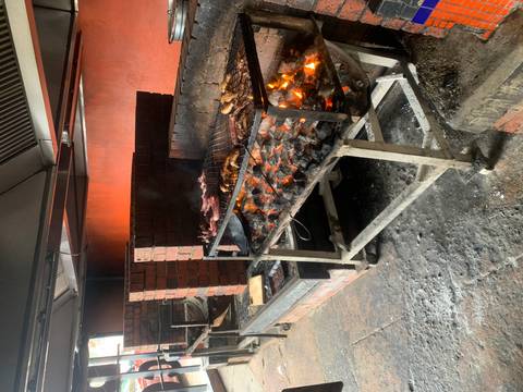       Indoor brick barbecue with glowing coals grilling various cuts of meat.
  