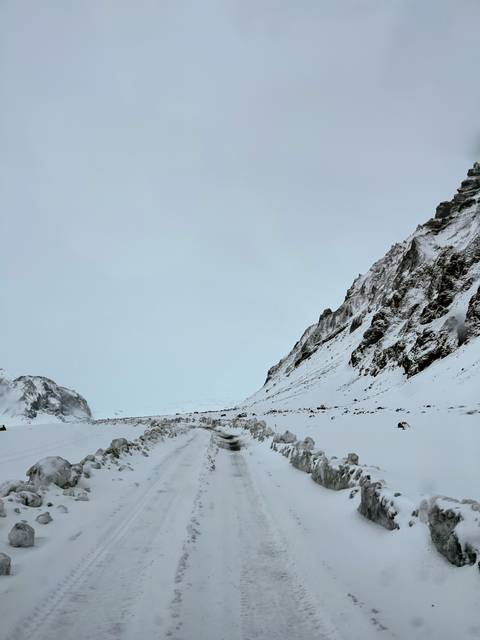       Snow-covered mountain slopes and a rough track under a pale overcast sky.
  