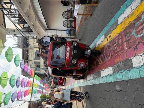       Colorful tuk-tuk drives along vibrant umbrella-covered street in San Juan La Laguna
  