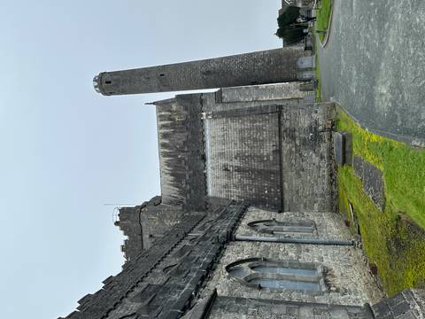       Stone cathedral with steep pitched roof and a tall medieval round tower rises over a quiet churchyard.
  