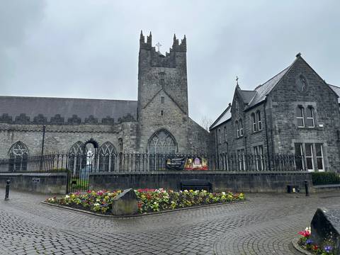       Grey-stone church and surrounding railings overlook a bright flowerbed on a damp morning.
  