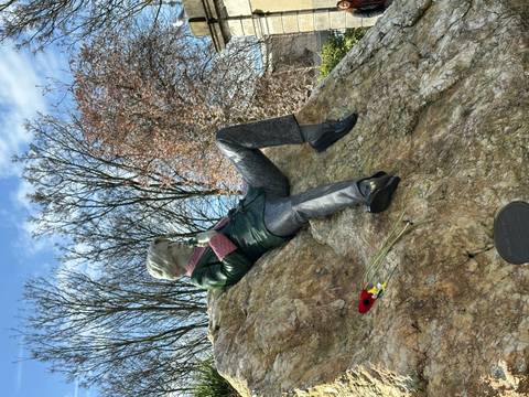       Colorful statue of Oscar Wilde reclines on a quartz boulder in a leafy city park.
  