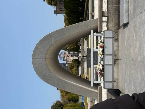       Stone arch cenotaph framing the Atomic Bomb Dome across a reflecting pond in Hiroshima Peace Memorial Park.
  