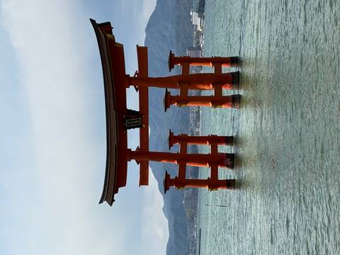      The iconic vermilion torii gate of Itsukushima Shrine standing in calm seawater with mountains behind.
  
