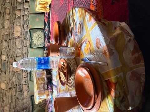       Simple meal setup with clay bowls, bread, tea glass and bottled water on a patterned plastic tablecloth.
  