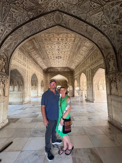       Smiling couple stands in an intricately inlaid marble hall with arched ceilings at Agra Fort.
  