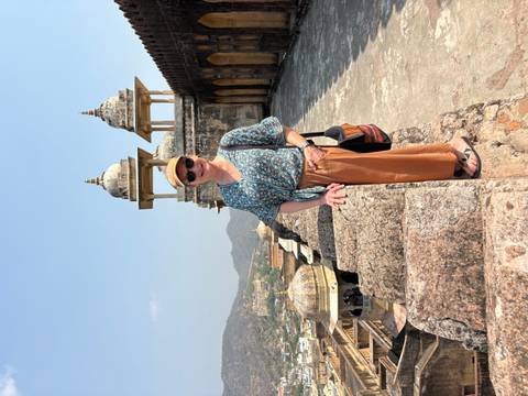       Traveller poses on the ramparts of Amber Fort overlooking arid hills and domed pavilions.
  