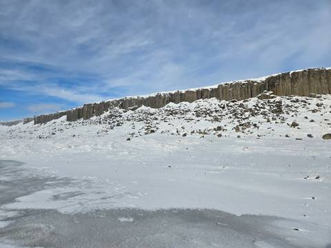       Rows of basalt columns rim a snowy Icelandic plateau beneath a blue sky
  