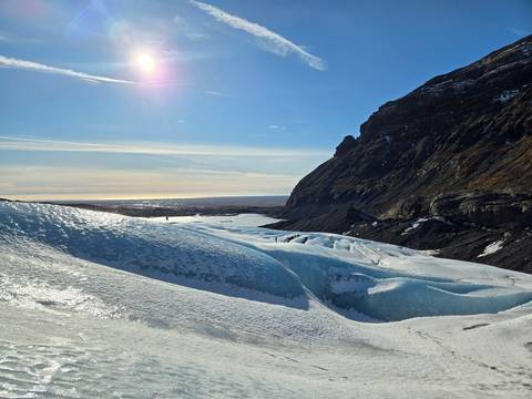       Blue glacial ice formations stretch toward distant ocean beneath rugged mountains
  