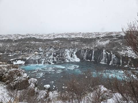       Snowy landscape with cascading Hraunfossar-style waterfalls into icy blue pool
  