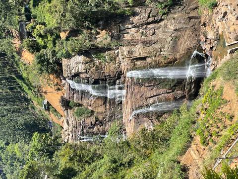       Tall multi-tiered waterfall cascading down rocky cliffs surrounded by lush green forest
  