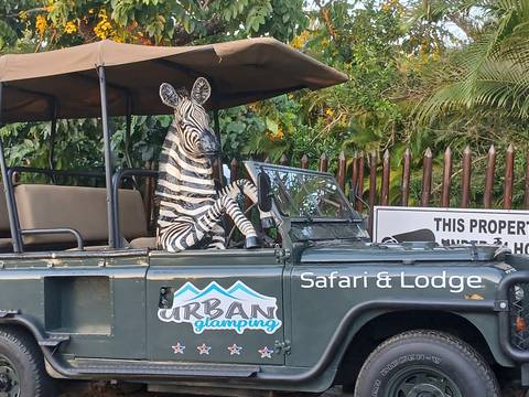       A safari jeep with a playful zebra mannequin seated behind the wheel outside a lodge entrance.
  