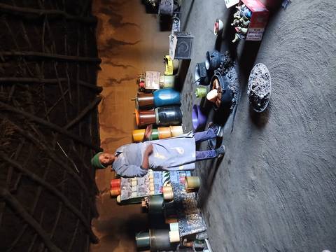       Local woman demonstrates traditional cooking over a small fire inside a thatched hut kitchen.
  