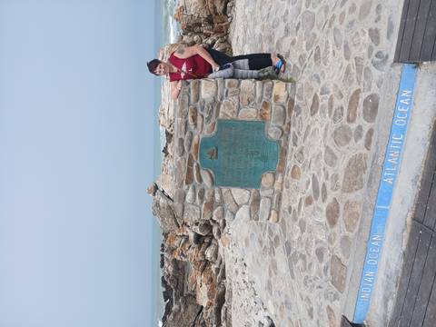       Traveller poses beside the Southern Tip of Africa monument at Cape Agulhas where two oceans meet.
  