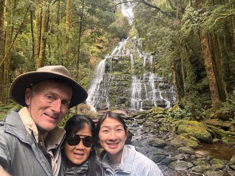       Family poses in front of a cascading rainforest waterfall surrounded by mossy rocks and trees.
  