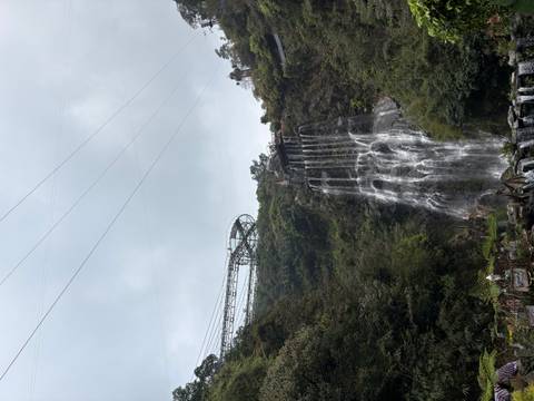       Tall waterfall cascading down cliff with sightseeing walkway and coaster track above
  