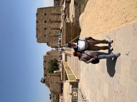       Travelers pose on the broad stone avenue of Karnak Temple with ruins and obelisks behind.
  