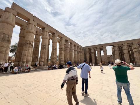       Visitors explore the vast courtyard of Luxor Temple lined by towering sandstone columns.
  