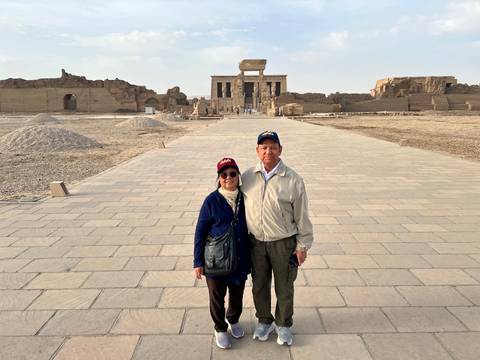       A couple stands on the broad paved approach to Dendera Temple with the sanctuary in the distance.
  