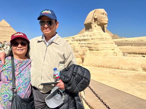       Travelers pose with the iconic Sphinx and Pyramid of Khafre rising behind under a clear blue sky.
  