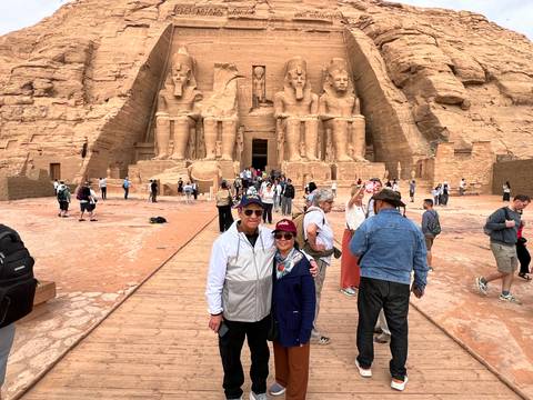       Tourists gather at the monumental façade of Abu Simbel with four seated Ramses II statues carved into rock.
  