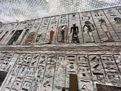       Detailed hieroglyphs and colorful deity figures adorn an ancient tomb wall under protective lighting.
  